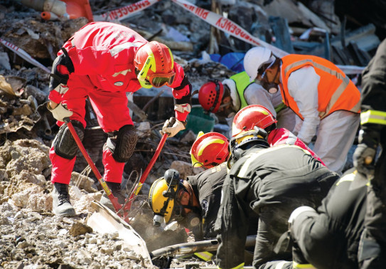 Crews wearing high visibility gear and hard hats work to break through the rubble left after the Christchurch Earthquake.