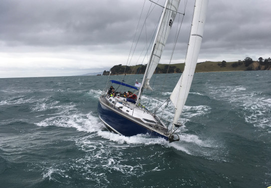 A Royal New Zealand Navy Sailing Training Craft sailing on the harbour on a grey cloudy day.