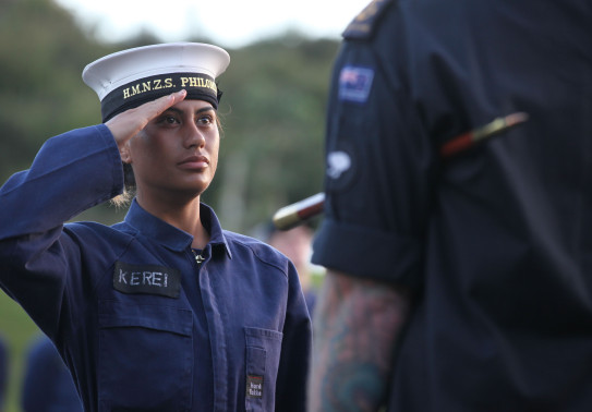 A Royal New Zealand Navy recruit salutes to another sailor (on back of them shown)