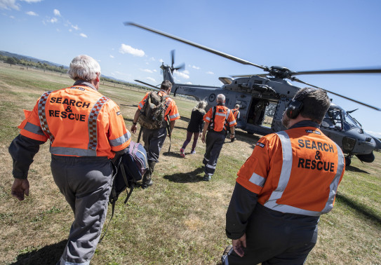 LandSAR personnel walk towards a Royal New Zealand Air Force NH90 helicopter on a nice day. 