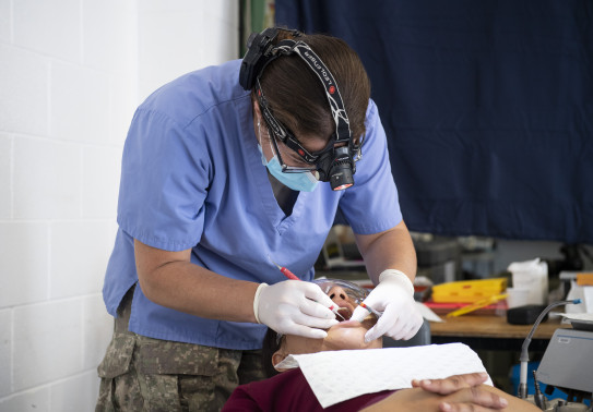 An NZDF dentist working on a patients mouth using a head torch. 