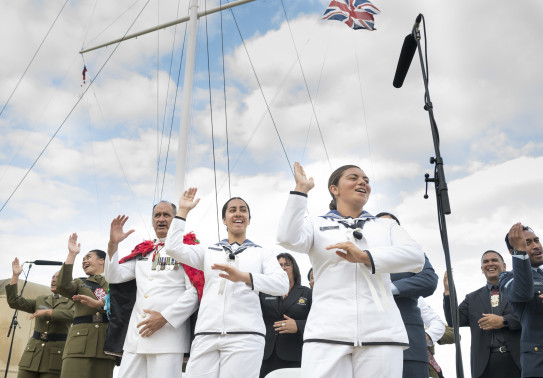 NZDF personnel perform and sing a waiata near a flag mask. Three Royal New Zealand Navy sailors are in the foreground. 