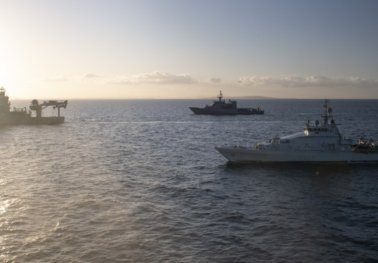 Three Royal New Zealand Navy ships sailing in the ocean HMNZS Otago, HMNZS Hawea and HMNZS Manawanui on a nice evening. There is some sun flare to the left of the image