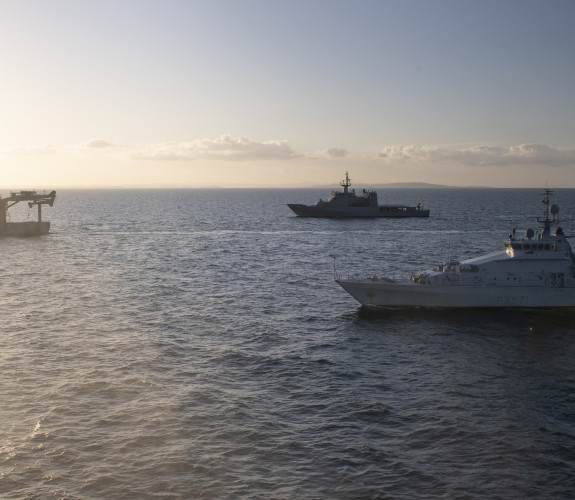Three Royal New Zealand Navy ships sailing in the ocean HMNZS Otago, HMNZS Hawea and HMNZS Manawanui on a nice evening. There is some sun flare to the left of the image