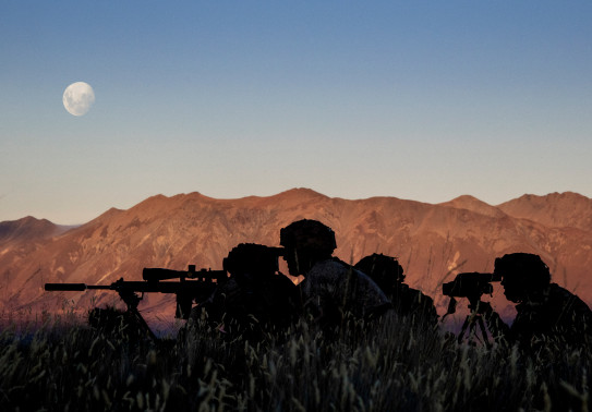 New Zealand Army soldiers using the Designated Marksman Weapon (DMW). The soldiers are silhouetted with the mountain range in the background lit up