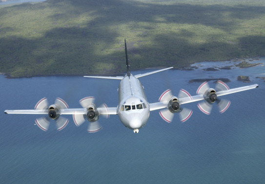 P-3K2 Orion flies over the ocean with land behind it. 