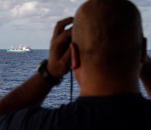 A sailor looks out of binoculars from the bridge of the ship to another boat.. 