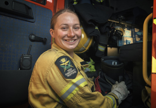 Sapper Danielle Brooks in a yellow firefighter jacket, smiling at the camera while standing beside a red firetruck