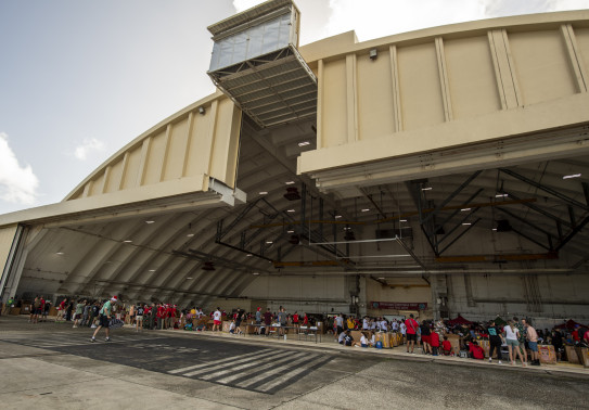 Personnel from a variety of countries pack bundles in a large aircraft hanger in Guam.