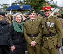 Proud Mum in a jacket and green scarf on the left, while the son and Dad (on the right) are in Army uniforms on the parade ground in front of other families and soldiers.