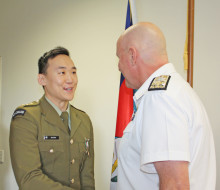 Captain Jin Cha in military dress uniform, receives the New Zealand Defence Service Medal from Commander Joint Forces New Zealand, Rear Admiral Jim Gilmour. The pair shake hands.