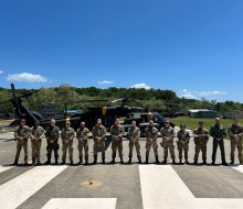 Uniformed personnel stand in front of a helicopter beneath blue skies.