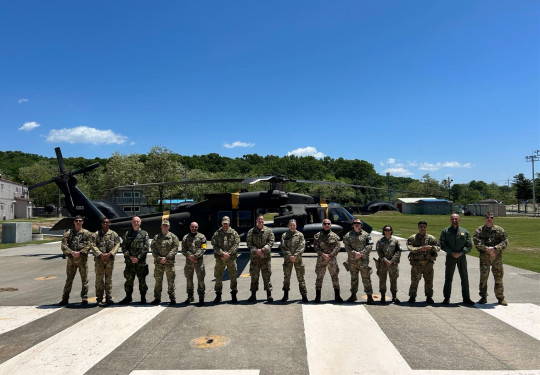 Uniformed personnel stand in front of a helicopter beneath blue skies.