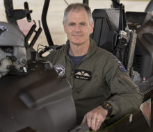 RNZAF Aviator sits in the cockpit of an aircraft staring at the camera. 