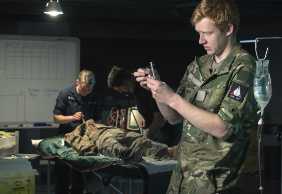 A New Zealand Army medic prepares to administer a patient with other medics behind attending to the patient