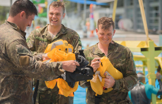 Solders from 3rd Combat Support support battalion smiling as they gather their life vests, packing up after escaping the submerged helicopter simulator
