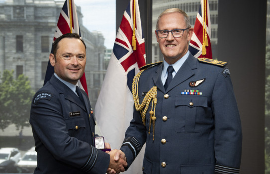 Squadron Leader Daniel Hayward and the Chief of Defence Force Air Marshal Kevin Short shake hands - in the background three flags