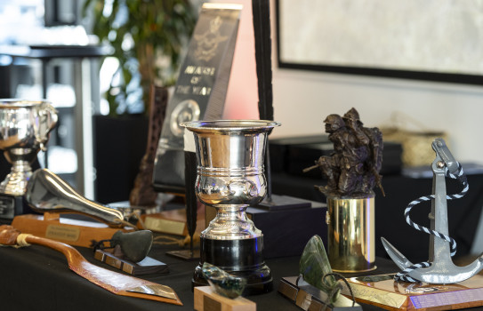 Photo of a tabletop upon which is arrayed a range of trophies and cups associated with NZDF Person of the Year awards.