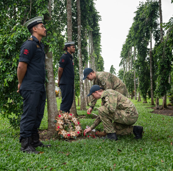 Two sailors stand at ease amongst the tree as two aviators place a wreath.