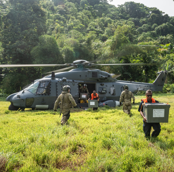 An NH90 helicopter in a field with dense forrest in the background as pilots and locals help deliver polling kits and ballot boxes to remote areas of the Solomon Islands.