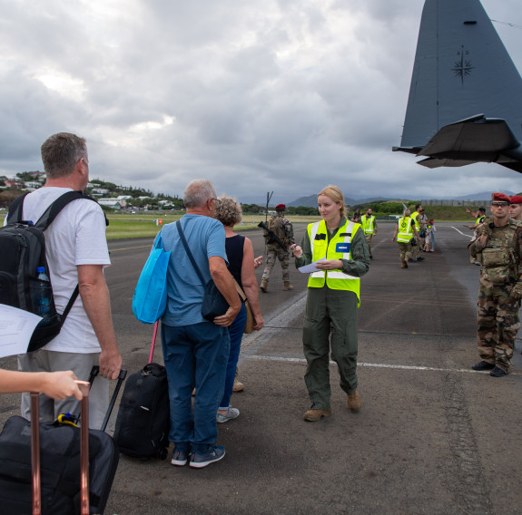 Personnel in high visibility jackets talk with civilians on the tarmac in front of the large grey C-130H (NZ) Hercules aircraft.