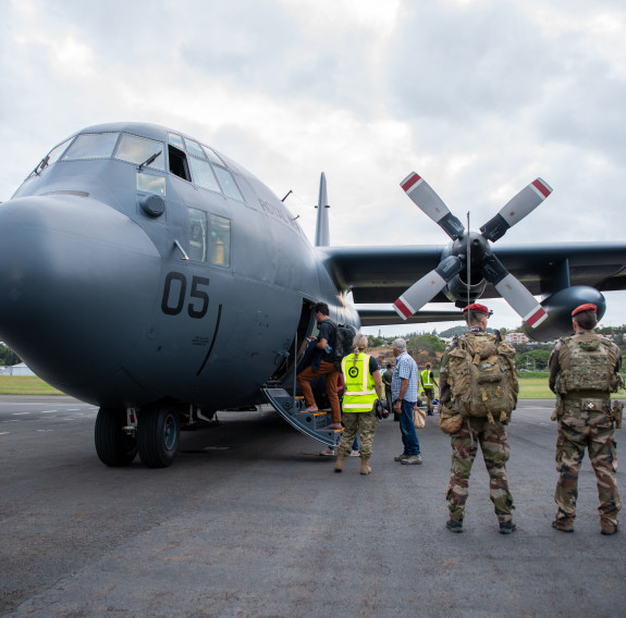 Front-on view of the Hercules aircraft. Local authorities watch on as people board the aircraft.