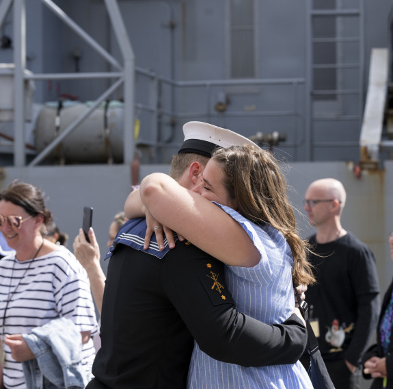 A sailor hugs a woman in front of a ship.