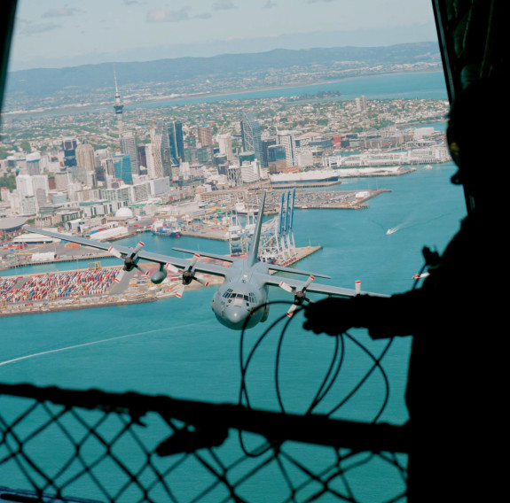 The view of Auckland City from the sky, out the back of a Hercules aircraft. Another RNZAF Herc flies behind, in front of the cityscape.