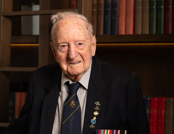 A man with medals on his blazer looks at the camera with books in the background.