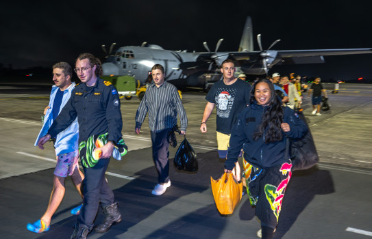 People walk across tarmac in front of a plane at night.