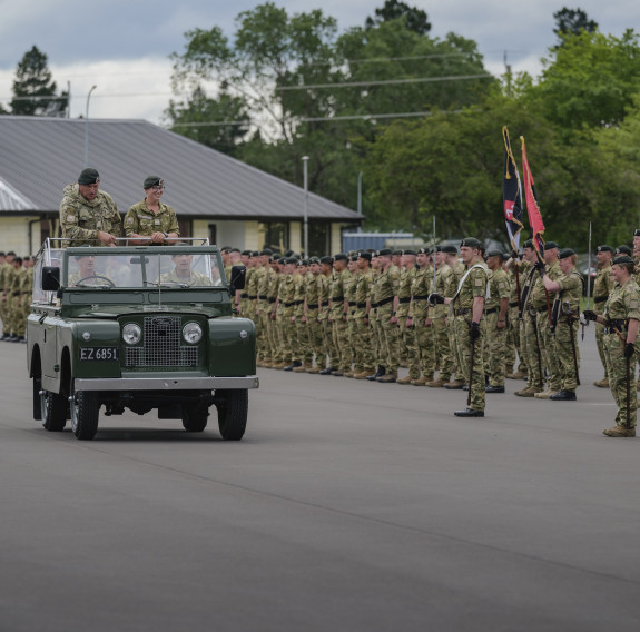 A car drives down a parade ground in front of soldiers standing in formation.