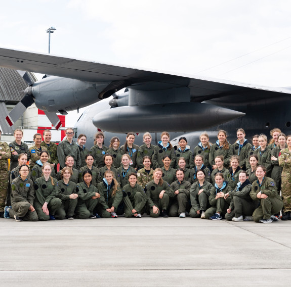 Students and Royal New Zealand Air Force personnel lined up for a photo underneath the wing of a C-130H(NZ) Hercules aircraft at Base Auckland.