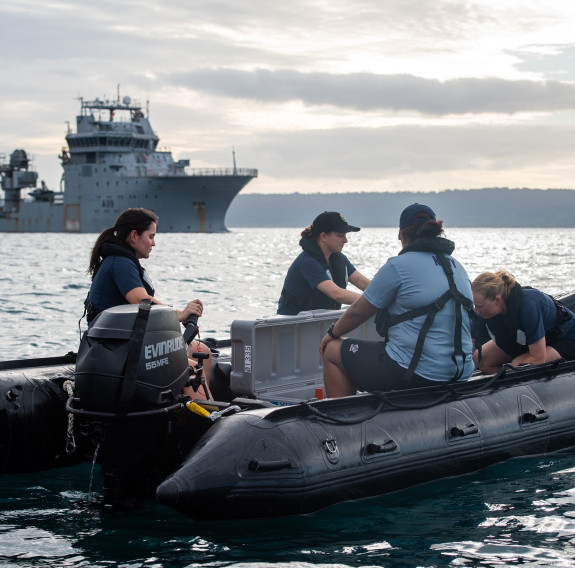 A RHIB with personnel on floats on the ocean with HMNZS Manawanui in the background.