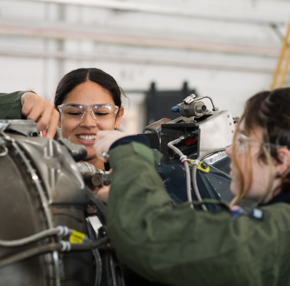 Two female students work on an engine of a small aircraft at the School to Skies camp.