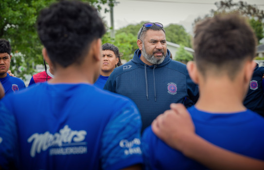 A man stands in the middle of a circle of young rugby league players.